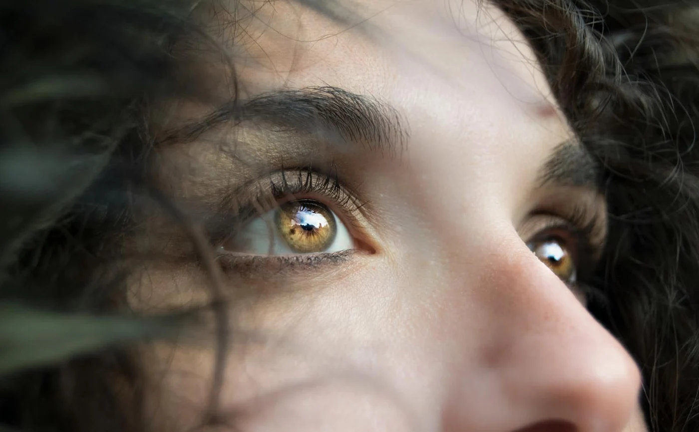 Close-up of an eye and upper face with curly hair in natural light.