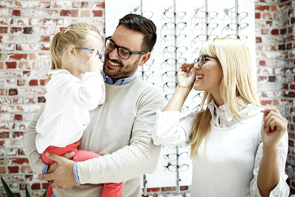 Two adults and a child trying on eyeglasses