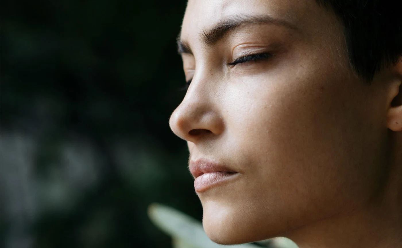 Natural side-profile portrait with a dark, softly blurred green background.